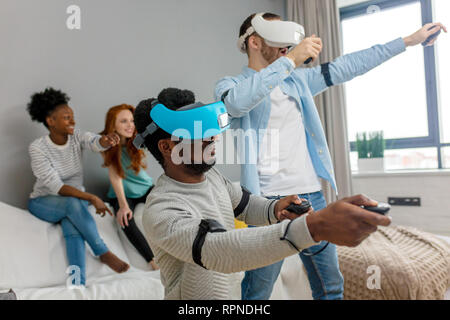 Gruppo di multirazziale maschio femmina amd gli studenti la riproduzione di gioco virtuale utilizzando occhiali VR, divertirsi insieme ay home - Virtual omg la realtà e portatile di Foto Stock