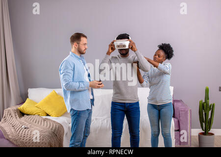 Foto di felice americano africano giovane e caucasico giovane uomo in piedi in camera e ridere mentre utilizzando 3d la realtà virtuale periferica. Foto Stock