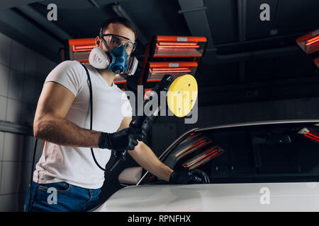 Dispositivo utile per la lucidatura di un'auto. close up foto. meccanico di indossare una maschera è in possesso di una lucidatrice e in posa per la fotocamera Foto Stock