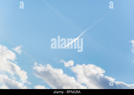 Aeroplano vola in nuvole bianche in un cielo blu e lasciando il sentiero. Foto Stock