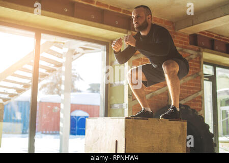 Giovane atleta maschio facendo salti plyo allenamento endurance in palestra crossfit. Il salto sulla scatola. Fase touchdown. Foto Stock