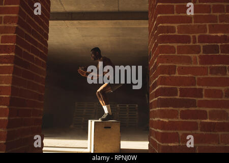 I giovani africani atleta maschio facendo salti plyo allenamento endurance in palestra crossfit. Il salto sulla scatola. Fase touchdown. Foto Stock