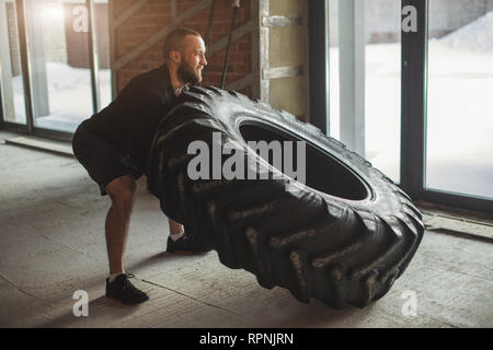 CrossFit tecnica dei pneumatici. Potente bodybuilder dimostra regole e ordine di formazione con improvvisato powerlifting elemento nel fitness club Foto Stock