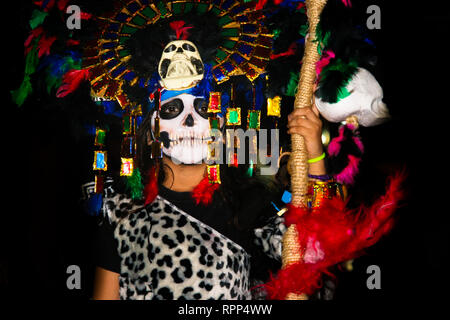 Ritratto di kid pesantemente camuffata con piume colorate e maya skull mask, indossando il costume di leopard, stando in piedi in strada durante la mexica annuale Foto Stock