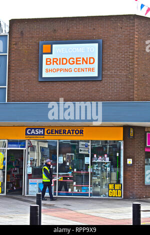 Segno di benvenuto fuori del moderno Bridgend Shopping Centre, sopra il generatore di cassa shop. Uomo in alta vis jacket passato a piedi. Foto Stock