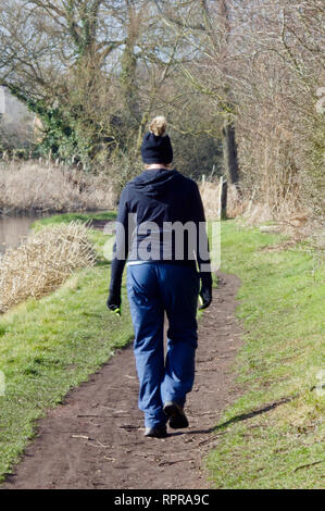 Di mezza età donna caucasica camminando lungo un canale Alzaia in inverno indossando un Bobble Hat Foto Stock