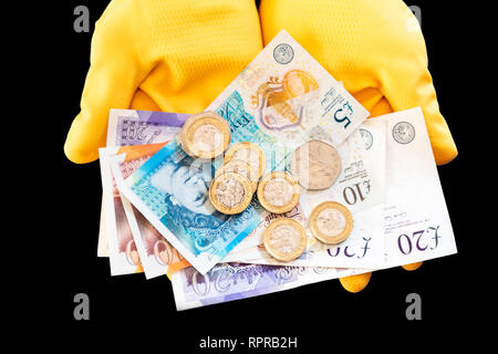 Una coppia di mani giallo da indossare guanti di gomma holding pound notes & monete. Concetto di contanti in mano, economia in nero o a bassa retribuzione. Foto Stock