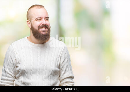 Giovani tanga caucasica uomo che indossa un maglione invernale su sfondo isolato che guarda lontano a lato con il sorriso sul volto, espressione naturale. Ridendo conf Foto Stock