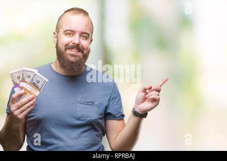 Giovane uomo parigamba holding mucchio di soldi su sfondo isolato molto felice rivolto con la mano e le dita per lato Foto Stock
