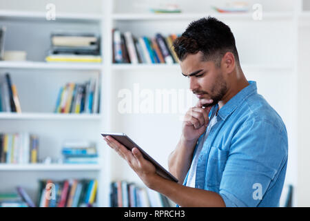 Pensando tanga messicano l uomo con la barba e tablet indoor a casa Foto Stock