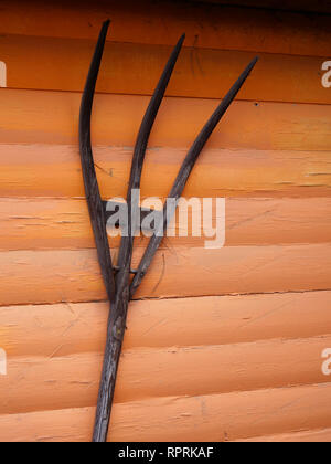 Un vecchio forcone di legno contro un luminoso dipinto di Orange muro del granaio Foto Stock