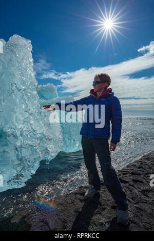 Persona esaminando un iceberg Breidamerkursandur sulla spiaggia di sabbia nera, al di sotto di Jokulsarlon. Sudhurland, sud est dell'Islanda. Foto Stock