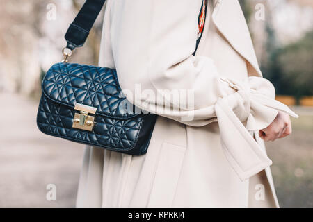 Primo piano di un nero Borsa trapuntata appeso alla spalla di una giovane donna che indossa un mantello bianco. Foto Stock