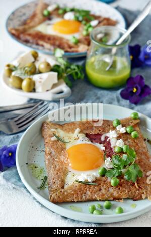 Il bretone tradizionale pancake fatti da farina di grano saraceno con prosciutto, formaggio, uovo, il formaggio feta, piselli verdi e burro verde. La prima colazione di grano saraceno frittelle sottili wi Foto Stock