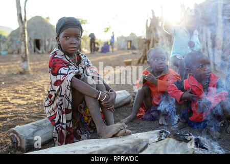 Bambini da tribù Zemba seduti intorno al fuoco in un tradizionale villaggio vicino a Epupa a sunrise, Namibia, Africa Foto Stock