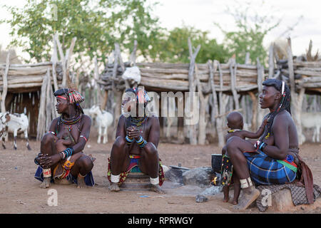 Persone provenienti da tribù Zemba seduti intorno al fuoco in un tradizionale villaggio vicino a Epupa, Namibia, Africa Foto Stock