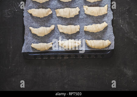 Materie croissant al cioccolato su una placca da forno prima della cottura. Vista dall'alto su sfondo scuro e pergamena bianca. Fly laici. Foto Stock