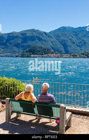 I turisti guardano a Bellagio da una panchina sulla riva del lago di Como, Lombardia, Italia Foto Stock