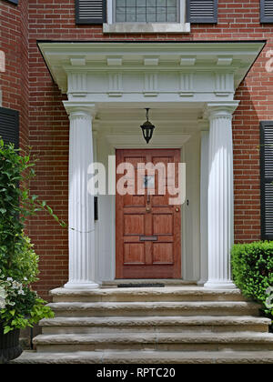 Portico di casa di mattoni con grandi colonne bianche, elegante porta in legno e gradini in pietra Foto Stock