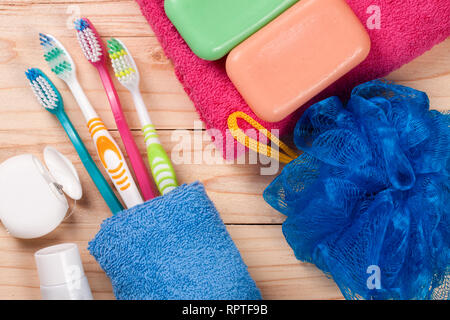 Gli spazzolini da denti, sapone, spugna e asciugamani su una tavola di legno. Prodotti igienici. Vista superiore Foto Stock