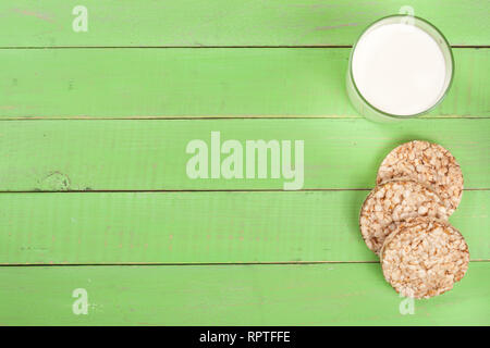 Un bicchiere di latte con fette biscottate di grano su un verde sullo sfondo di legno con una copia dello spazio per il tuo testo. Vista superiore Foto Stock