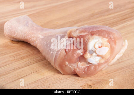 Un greggio di coscia di pollo su un tagliere di legno Foto Stock