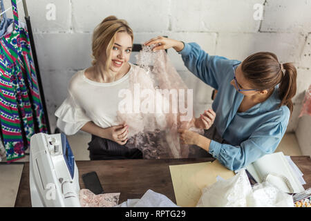 Giovane bella donna bionda sceglie il tessuto per il suo abito da sposa e femmina sarto professionale in Elegante camicetta blu aiuta nel suo Foto Stock