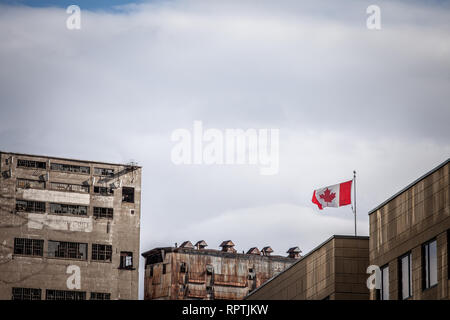 Bandiera canadese la rinuncia di fronte a una vecchia zona industriale fatta di abbandono dei silos, fabbriche e magazzini sul porto di Montreal, Quebec, Canada, chiuso Foto Stock