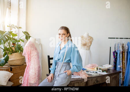 Femmina creativo sarta, vestito in Elegante camicetta e pantaloni dritti con nastro di misurazione sorridente piacevolmente lavora con fantoccio in stile vintage Foto Stock