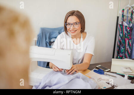 Giovane donna sarta cuce sulla macchina da cucire. Sarta lavorando sulla macchina da cucire, rendendo un vestiti nel suo posto di lavoro. Hobby cucito come una piccola bu Foto Stock