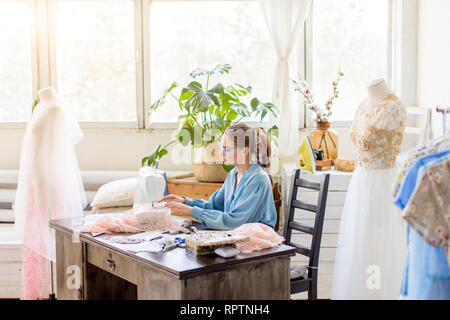 Giovane donna sarta cuce sulla macchina da cucire. Sarta lavorando sulla macchina da cucire, rendendo un vestiti nel suo posto di lavoro. Hobby cucito come una piccola bu Foto Stock