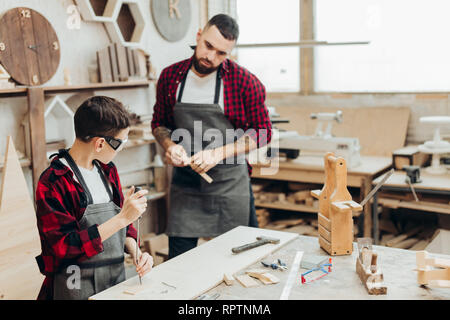 Padre e figlio in officina armeggiare giocattolo di legno. Papà insegnamento piccolo figlio di riparazione. La paternità e la condivisione di esperienze di concetto. Insegnante con ki maschio Foto Stock