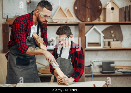 Relazioni familiari, la paternità, hobby, falegnameria, concetto di falegnameria - padre e figlio la riproduzione di cavalieri con legno spade DIY al workshop di falegname Foto Stock