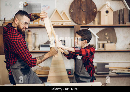 Relazioni familiari, la paternità, hobby, falegnameria, concetto di falegnameria - padre e figlio la riproduzione di cavalieri con legno spade DIY al workshop di falegname Foto Stock