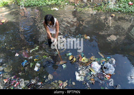 23/02/2019 di Cebu City, Filippine. Una donna wades in acqua torbida cercando di rimuovere accummulated cestino nel fiume. Foto Stock