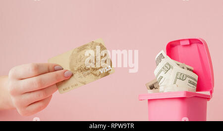 La carta di credito in una donna di mano e dollari in un cestino a sfondo rosa. Foto Stock