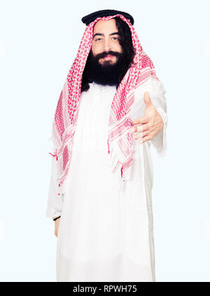 Arabian business man con capelli lunghi indossando il tradizionale keffiyeh sciarpa sorridente cordiale offrendo stretta di mano come saluto e accogliente. Busin di successo Foto Stock