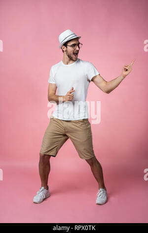 Attraente sorridente giovane dito del braccio che mostra di spazio vuoto in soli hanno segnale look casual da indossare t-shirt bianco isolato su sfondo rosa. Foto Stock