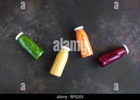 Vari frullati colorati o di succhi di frutta in bottiglie sul buio. Una sana dieta vegana detox alimenti puliti concetto, vista dall'alto, copia dello spazio. Foto Stock