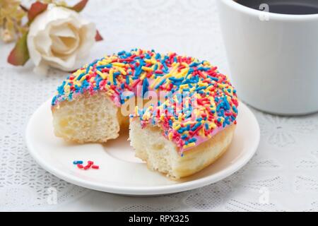 Tazza di caffè e una metà mangiato ciambella con un pizzico Foto Stock