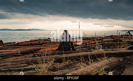 Donna seduta sulle rocce che guarda al mare, British Columbia, Canada Foto Stock