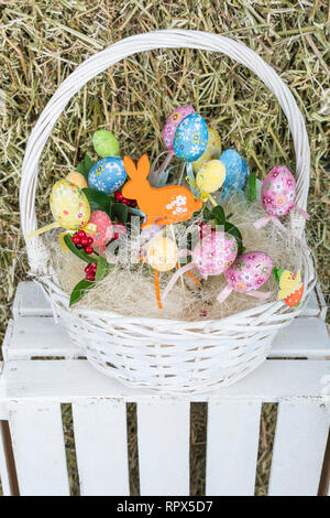 In vimini cesto bianco con un bouquet di uova di pasqua in una scatola di legno su uno sfondo di paglia Foto Stock