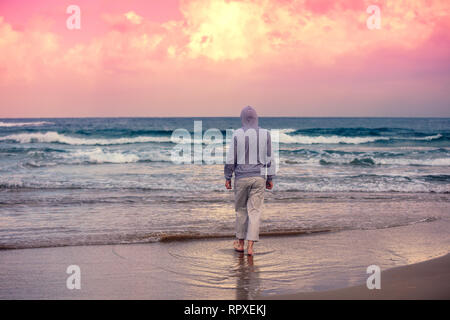 Un uomo cammina a piedi nudi sulla spiaggia e orologi di un magico tramonto Foto Stock