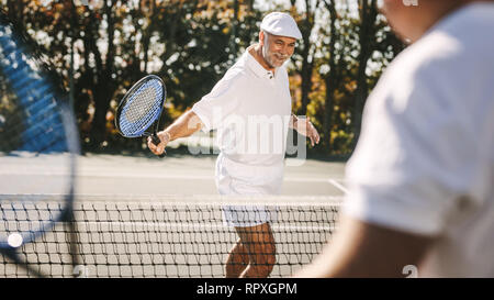 Allegro alti uomini godendo di una partita di tennis all'aperto. Sorridente uomo senior in usura tennis giocando a tennis con un amico. Foto Stock