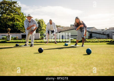 Le persone che giocano una partita a bocce in un prato in una giornata di sole. Due persone anziane la piegatura in avanti gettando le bocce in concorrenza gli uni con gli altri. Foto Stock