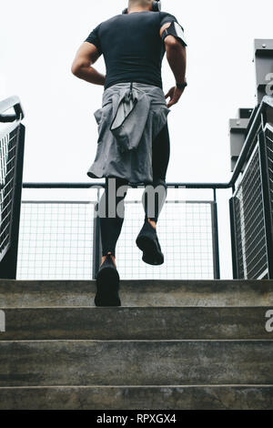 Vista posteriore del giovane uomo correre su per i gradini. Montare l'uomo in abbigliamento sportivo lavorando sulle scale. Foto Stock