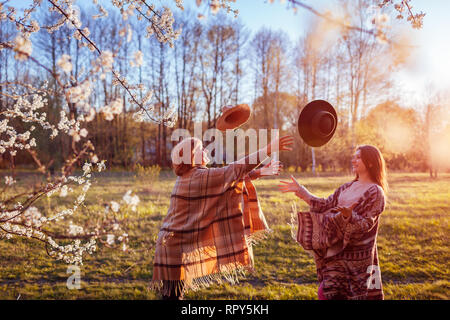 Felice senior mamma e figlia adulta gettando cappelli in giardino di primavera al tramonto. La festa della mamma concetto. Le donne avendo divertimento Foto Stock