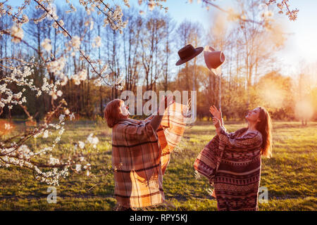 Felice senior mamma e figlia adulta gettando cappelli in giardino di primavera al tramonto. La festa della mamma concetto. Le donne avendo divertimento Foto Stock