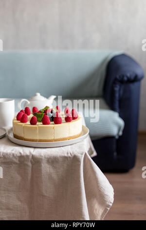 Cheese Cake con frutti di bosco sul tavolo con la tovaglia, il divano in background Foto Stock