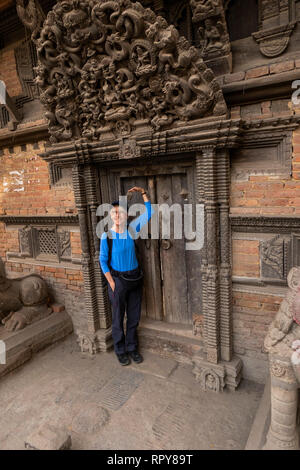 Il Nepal, Kathmandu, centro città, Jyatha Marg, Chhusya Bahal, senior piccolo turista femminile sotto antiche torana scolpita sopra la porta del tempio Foto Stock